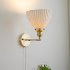 This Clérachic wall light with its pleated ceramic shade turned upward on an elbow brass arm, throwing light up a pale wall.