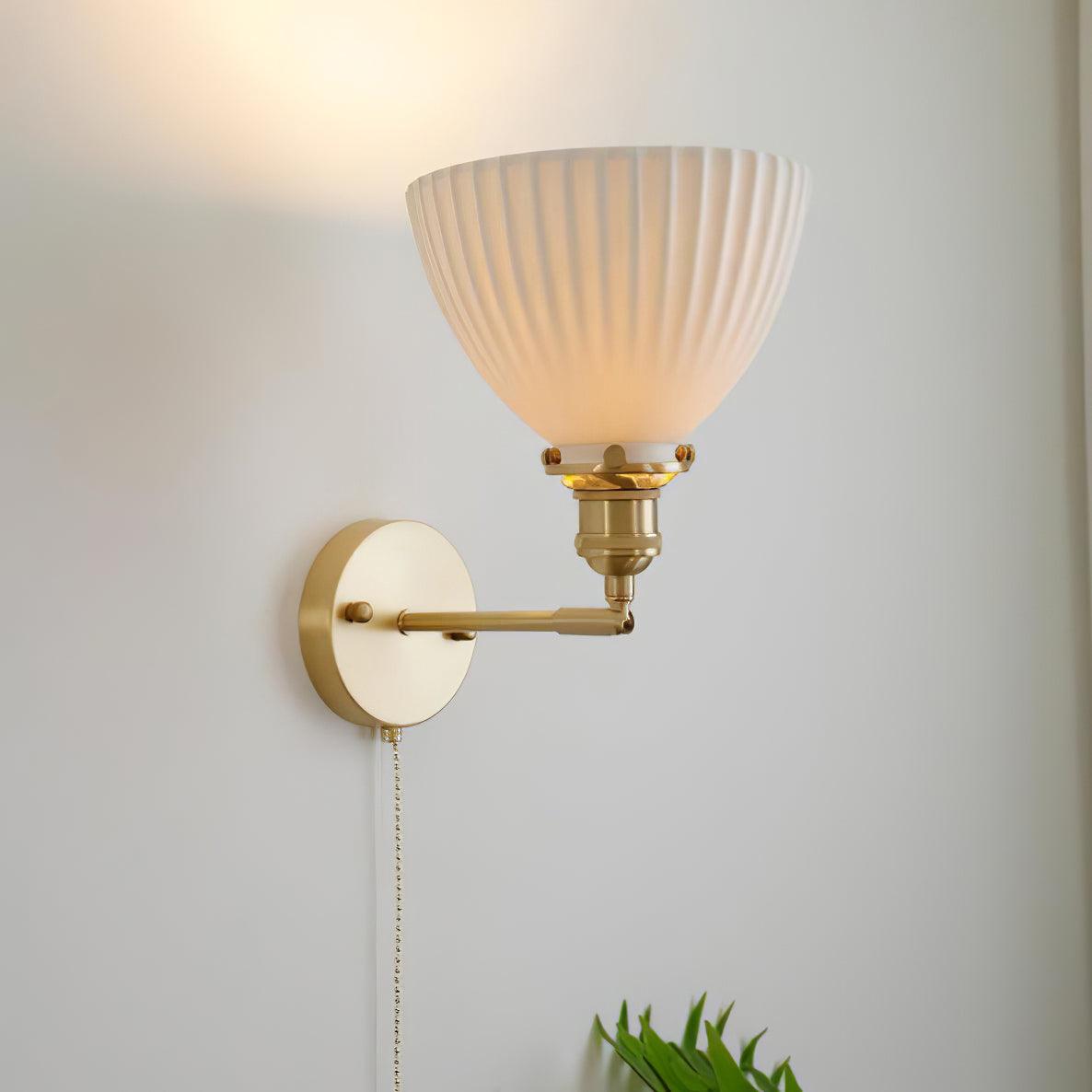This Clérachic wall light with its pleated ceramic shade turned upward on an elbow brass arm, throwing light up a pale wall.