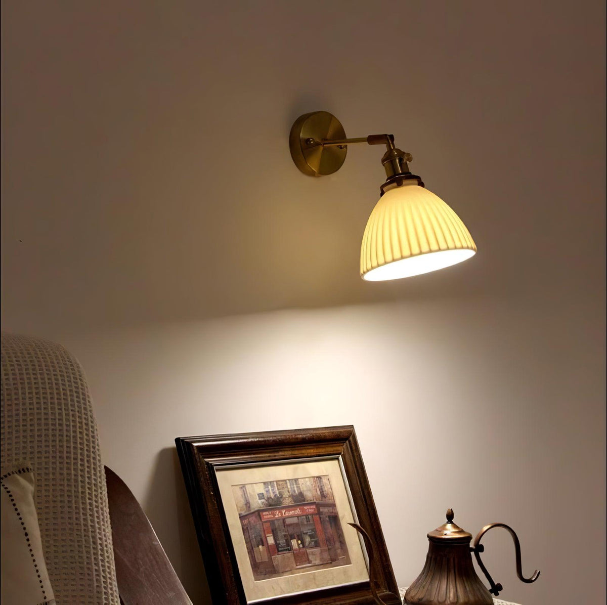 Clérachic wall light glowing above a framed print and a copper kettle on a bedside table, in a warm beige bedroom.