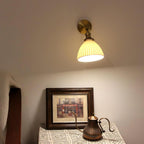 A Clérachic ceramic wall light lit above a framed street scene and a dark metal kettle on a lace-covered table.