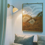 Small Clérachic wall light with a pleated shade beside a large framed abstract artwork, above grey-green cushions on a sofa.