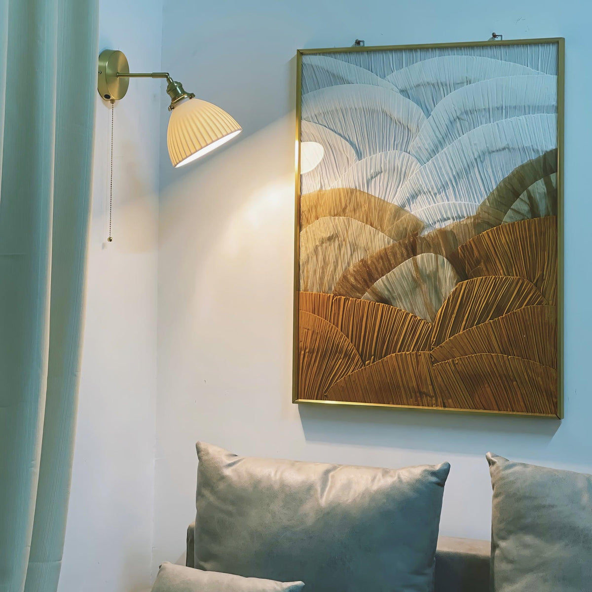 Small Clérachic wall light with a pleated shade beside a large framed abstract artwork, above grey-green cushions on a sofa.