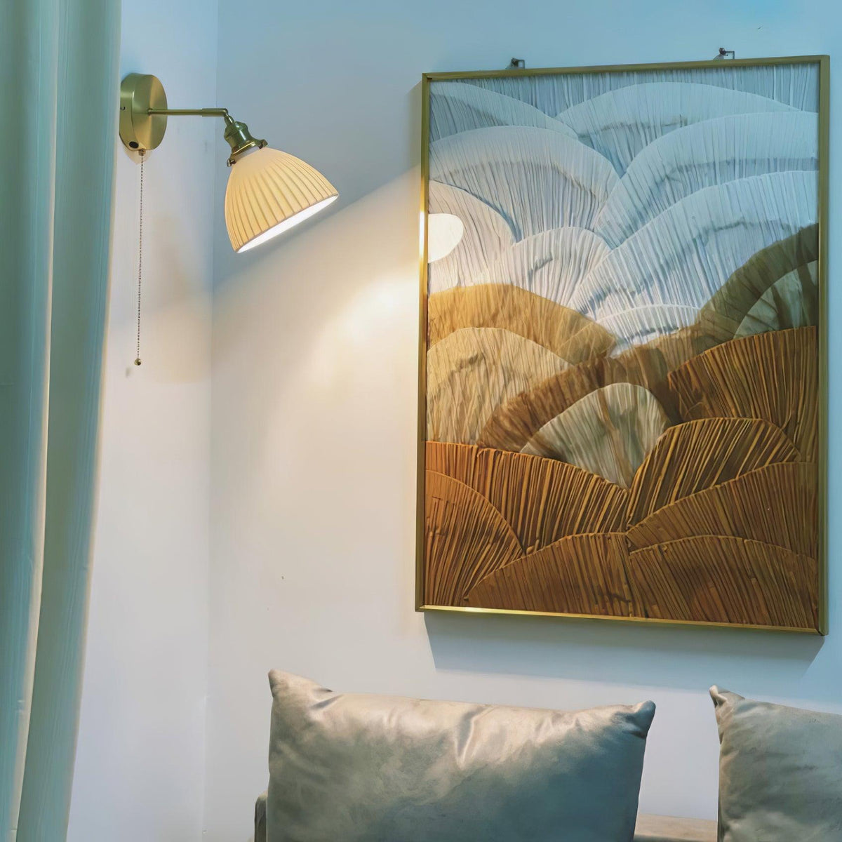 A Clérachic ceramic wall light mounted on a pale wall next to a gold-framed painting and a sofa with grey-green cushions.