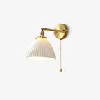 This Clérachic wall light on a plain off-white backdrop, its brass arm, pleated white shade and bead pull chain clear.