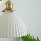 Close view of the brass socket and thumb screw above the pleated ceramic shade of this Clérachic wall light, a fern behind.