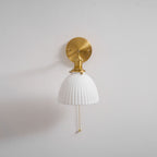 Bell-shaped pleated ceramic shade under a brass fitting, this Clérachic wall light shown head-on with its chain hanging down.