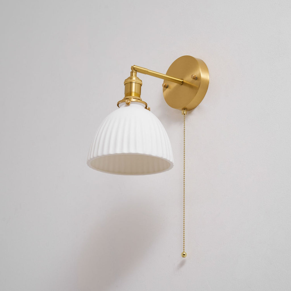 Clérachic wall light with a wide ribbed ceramic shade and an angled brass arm, shown unlit against a soft grey wall.