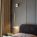 Beside a grey padded headboard and gold-toned curtain, this Clérachic brass wall light casts a warm pool of light downward.