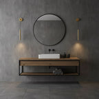 Two brass tube wall lights on either side of a round black mirror above a wood-and-steel vanity, a Clérachic wall light.