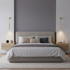 Brass tube wall lights frame a bed with a beige headboard, light falling softly onto the pale bedside units, from Clérachic.