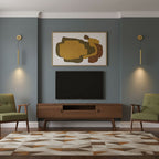 Two brass wall lights on a blue-grey wall flank a framed abstract print above a wooden media unit, a Clérachic wall light.