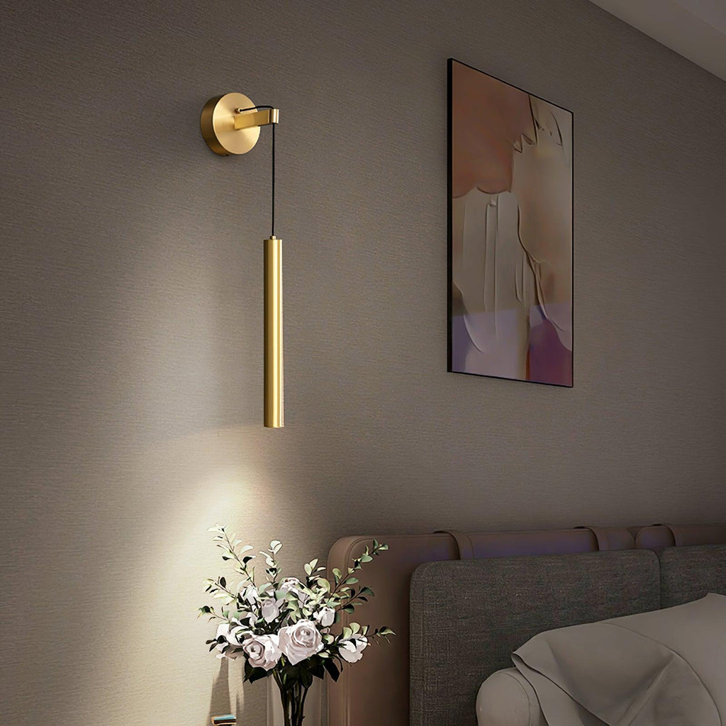Brass tube wall light beside a framed print above a bed, with a vase of white roses below catching the light, from Clérachic.