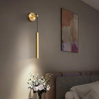 Brass tube wall light beside a framed print above a bed, with a vase of white roses below catching the light, from Clérachic.