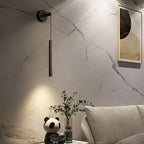 Black tube wall light on a white marble-effect wall above a sofa with a panda figure and green plant, from Clérachic.