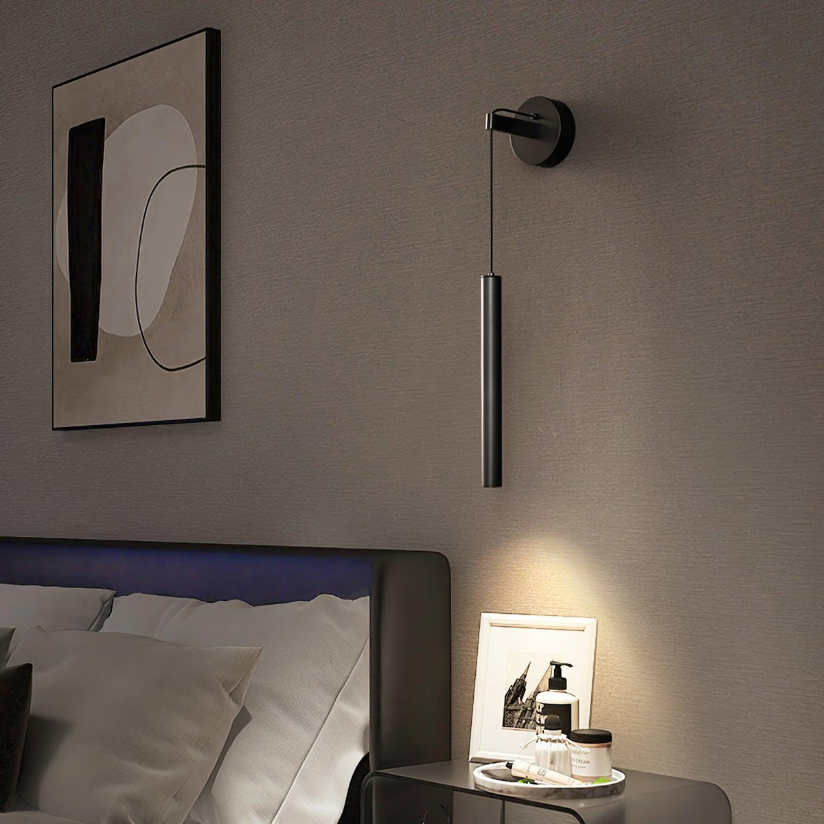 Black tube wall light beside an abstract framed print above a bed and glass bedside table, from Clérachic.