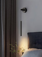 Black wall light on a pale wall beside a heavy grey curtain and a woven headboard, with a warm glow below, from Clérachic.