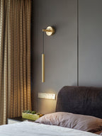 Brass wall light hangs in a bedroom with a brown textured curtain and a grey headboard, a warm glow beneath, from Clérachic.