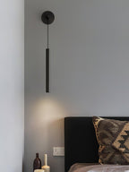Black wall light above a bed with a woven patterned cushion and glass bottles on the side table, a Clérachic wall light.