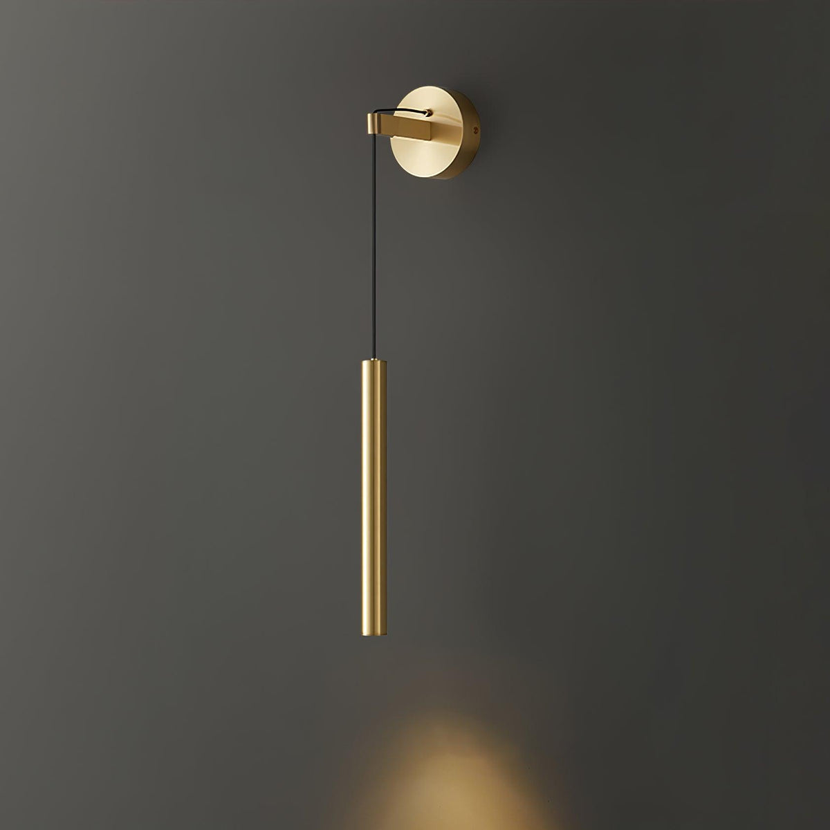 Brass tube on a black cord hangs from a brass backplate on a dark grey wall, with a warm spot of light below, from Clérachic.