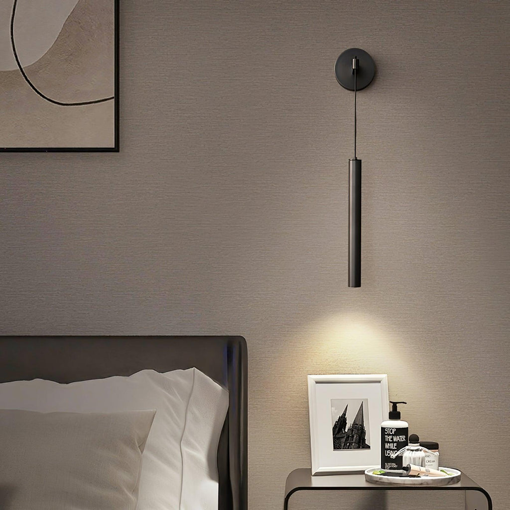 Black wall light over a glass bedside table with a framed photo and toiletries, light pooling on the wall, a Clérachic wall light.