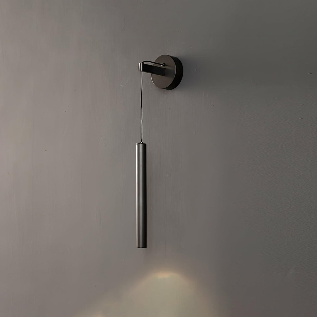 Black tube wall light on a charcoal wall with a warm cone of light spreading below it, a Clérachic wall light.