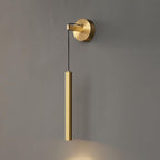 Brass tube wall light on a grey wall, with a warm wash of light on the wall beneath it, from Clérachic.