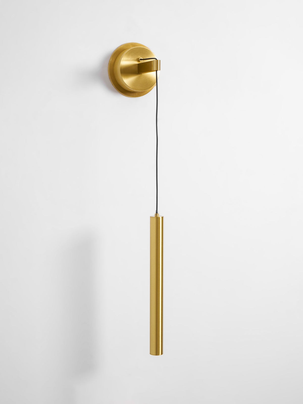 Brass wall light with a round backplate and slim tube against a pale wall, seen slightly from the side, a Clérachic wall light.