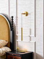 Brass wall light on a white panelled wall above a black bedside table with a candle and a gold dish, from Clérachic.