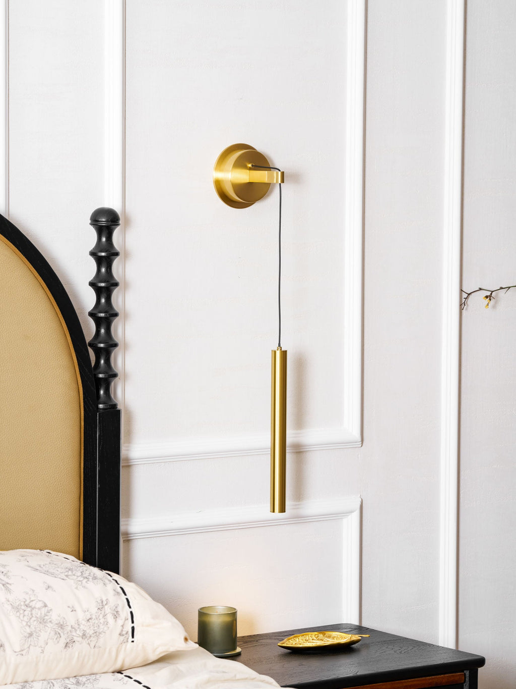 Brass wall light between white wall panels, with an arched headboard and a black carved bedpost beside it, a Clérachic wall light.