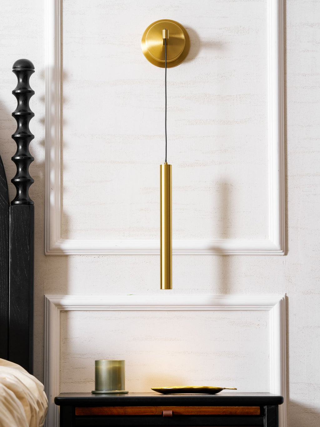 Brass wall light above a dark wooden bedside table, set against white wall mouldings, from Clérachic.