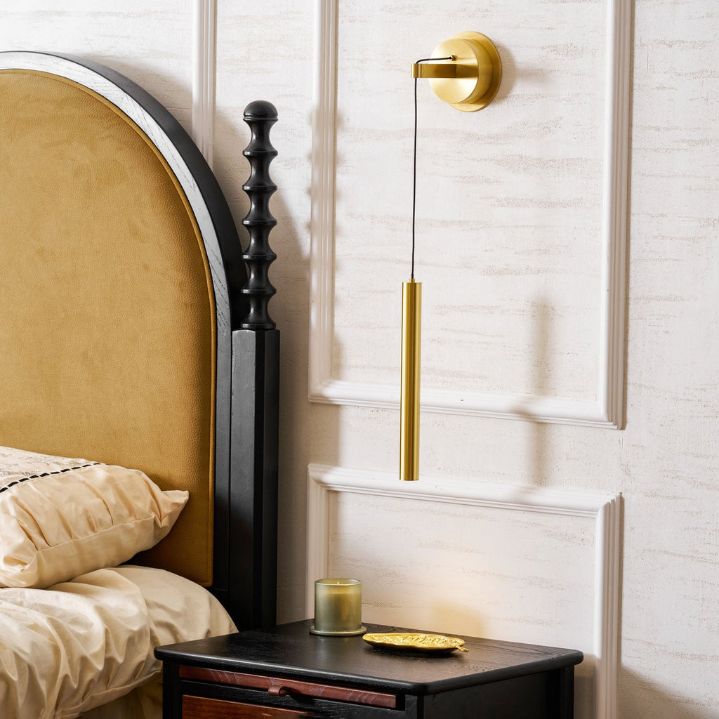 Brass wall light beside an arched velvet headboard and a carved black bedpost, on a white panelled wall, from Clérachic.