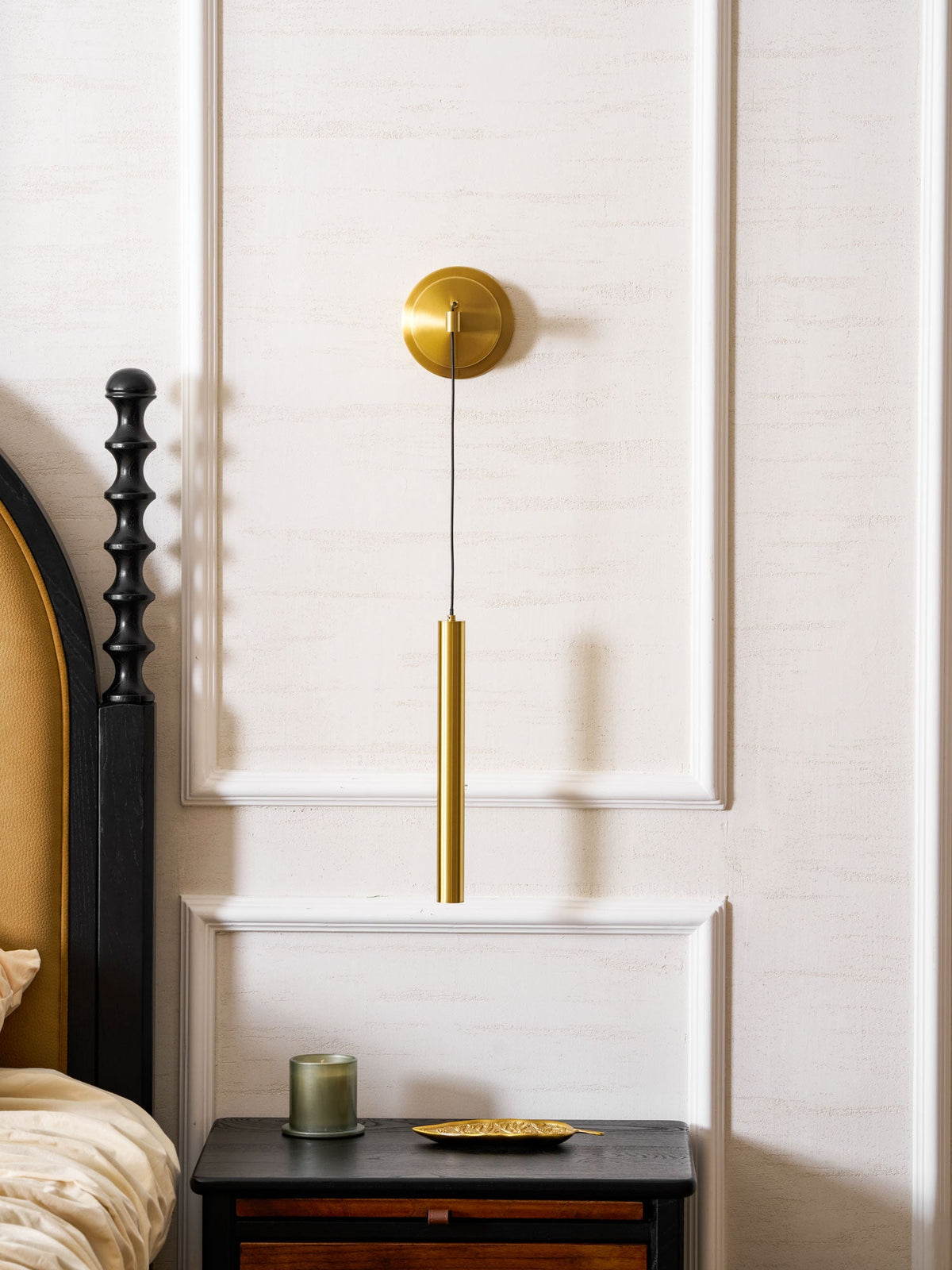 Brass wall light centred on a white panelled wall above a dark bedside table, a Clérachic wall light.
