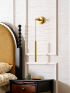 Brass wall light with its cord and tube beside an arched headboard, a black bedside table beneath, from Clérachic.