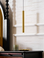 Lower section of a brass tube above a green glass candle and gold dish on a black bedside table, a Clérachic wall light.