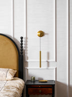 Brass wall light on a white panelled wall beside an arched headboard and a bedside table with a scalloped drawer, from Clérachic.