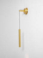 Brass wall light seen from a slight angle on a pale wall, showing the arm, cord and tube, a Clérachic wall light.