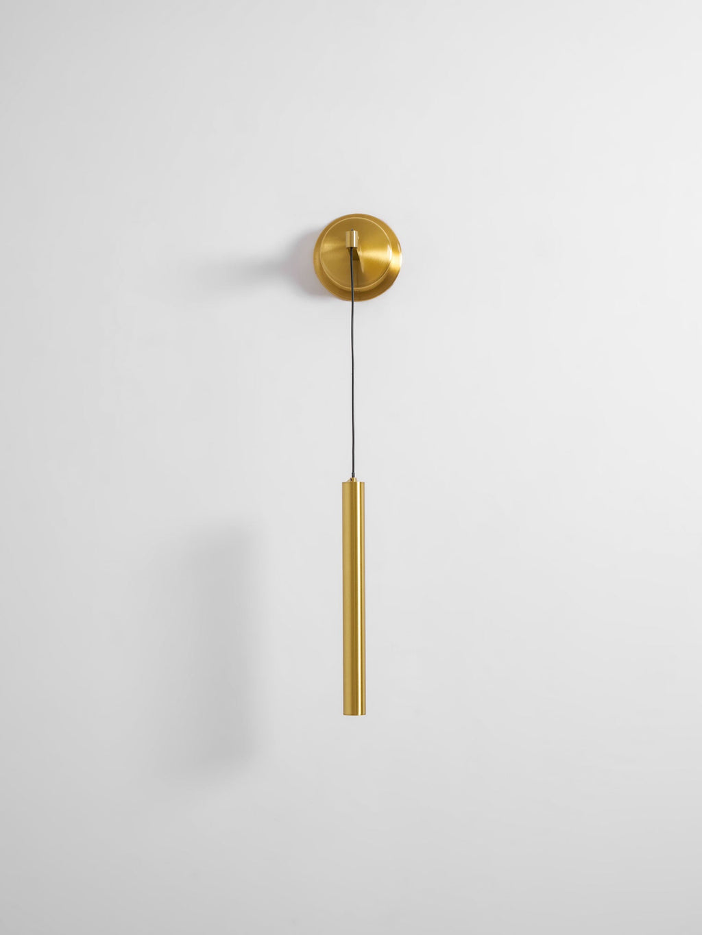 Small brass wall light with a slim tube on a pale wall with plenty of empty space around it, from Clérachic.