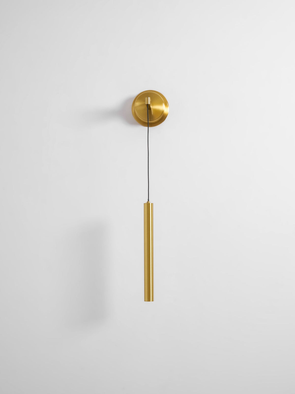 Small brass wall light with a slim tube on a pale wall with plenty of empty space around it, from Clérachic.