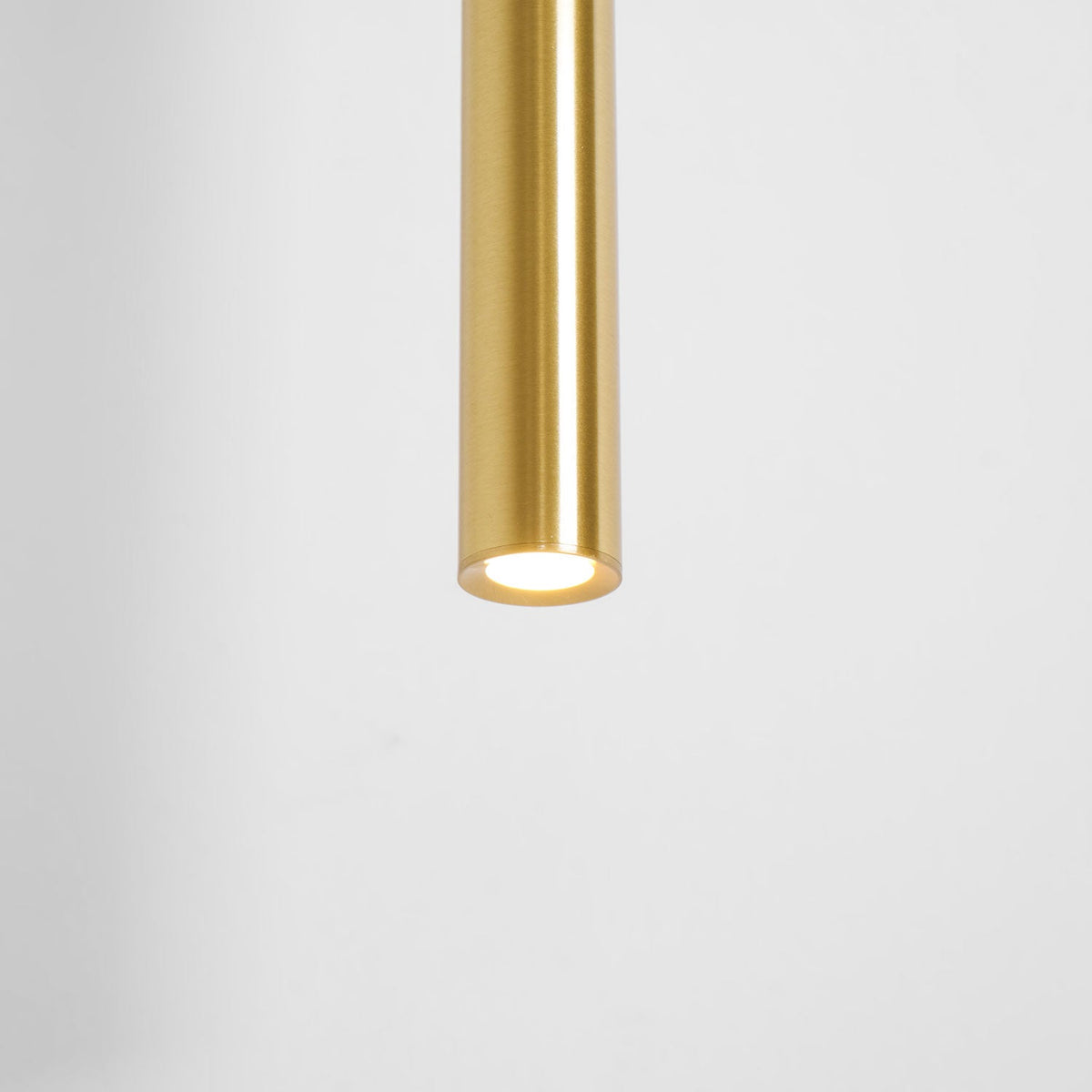 Underside of the brass tube with its LED lit, against a white wall, on this Clérachic wall light.