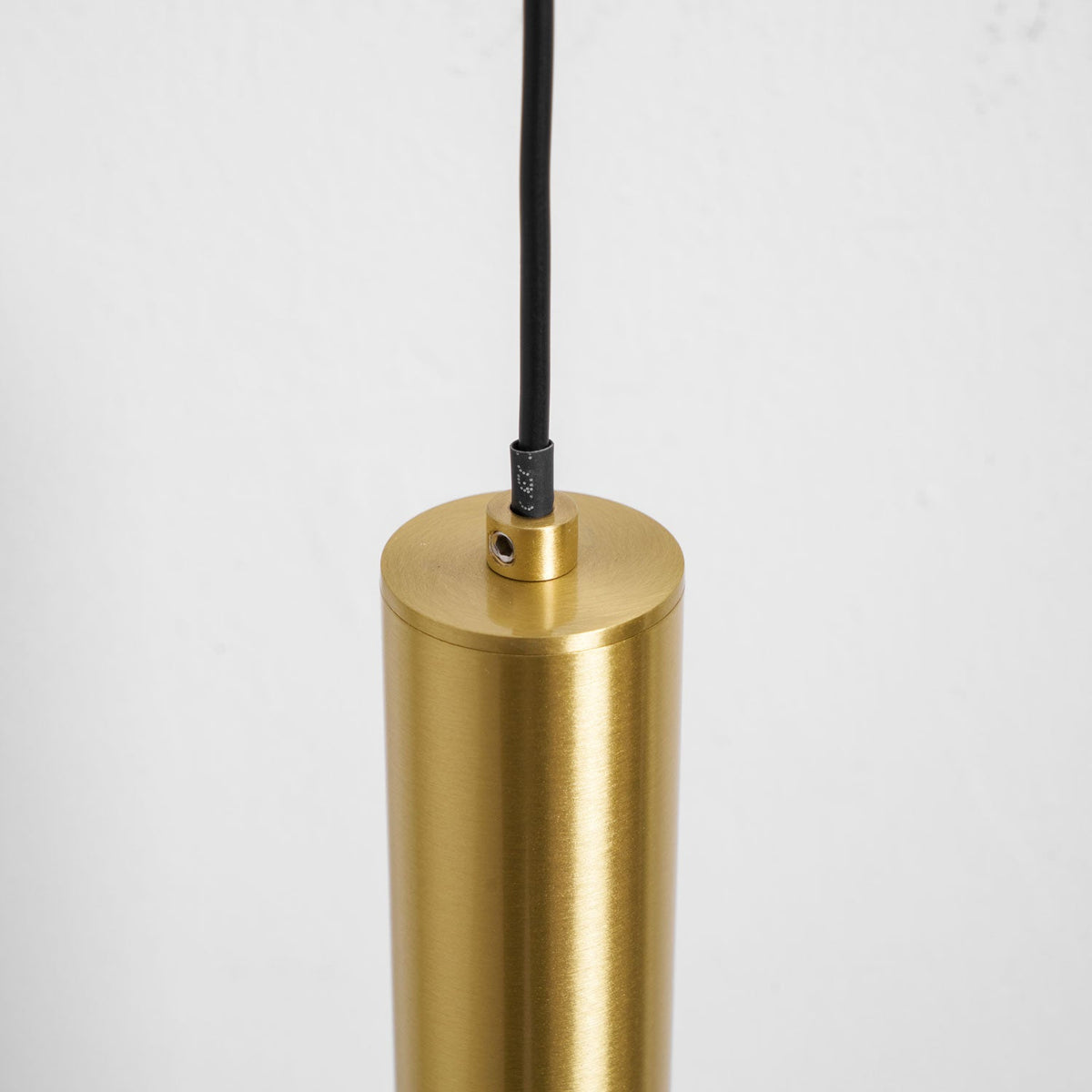 Close view of the top of the brass tube where the black cord enters, with a small fixing screw, on this Clérachic wall light.