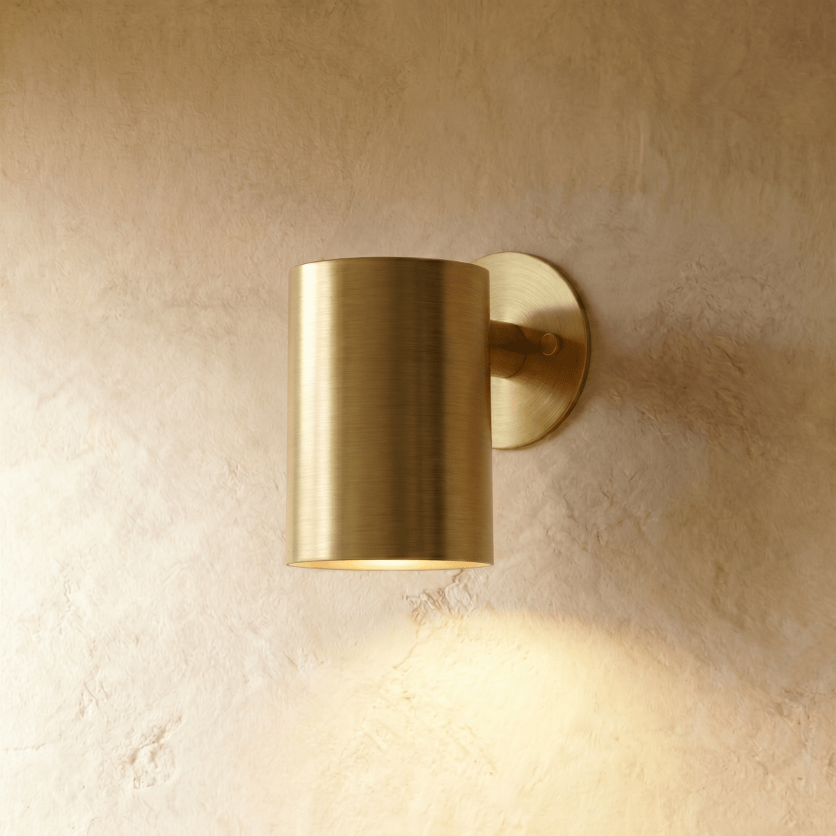 This Clérachic cylindrical wall light in polished brass throws a warm downlight over a textured plaster surface.