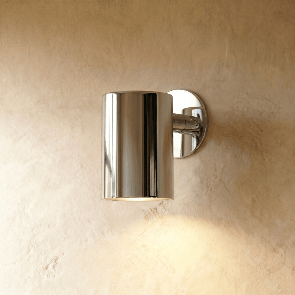 This Clérachic cylindrical wall light in mirror-polished chrome reflects the room against a textured plaster wall.