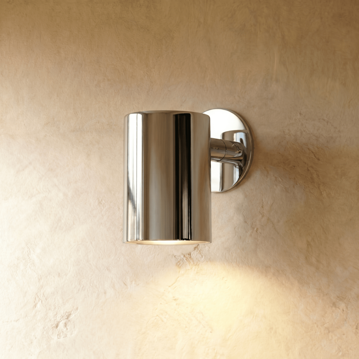 This Clérachic cylindrical wall light in mirror-polished chrome reflects the room against a textured plaster wall.