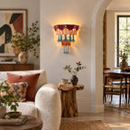 A lit Clérachic wall sconce on a cream wall beside an arched doorway, with a boucle sofa and a rustic stump side table below.