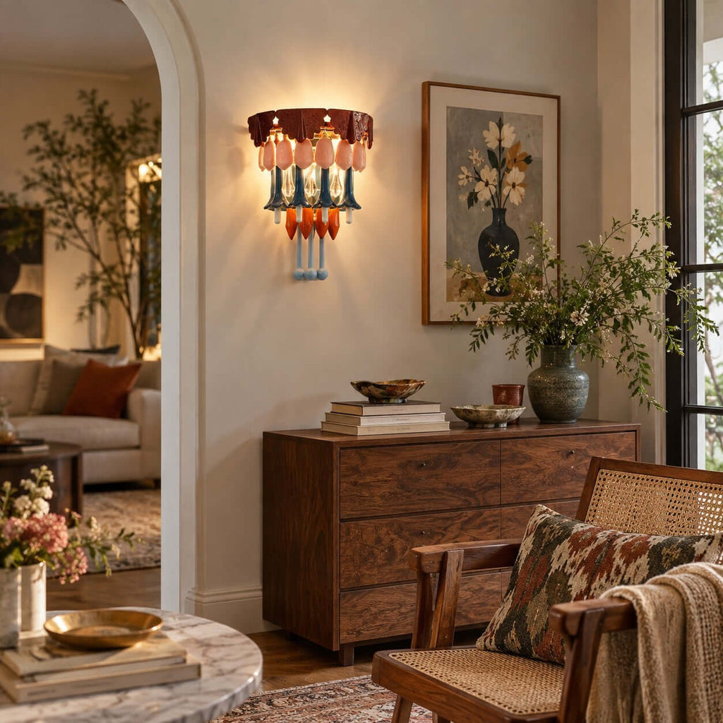 Beside a framed vase print, a Clérachic wall sconce casts warm light over a walnut chest, a rattan armchair and a leafy branch.