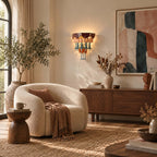 A Clérachic wall sconce on a pale wall beside tall windows, over a walnut sideboard and a curved boucle armchair on a woven rug.