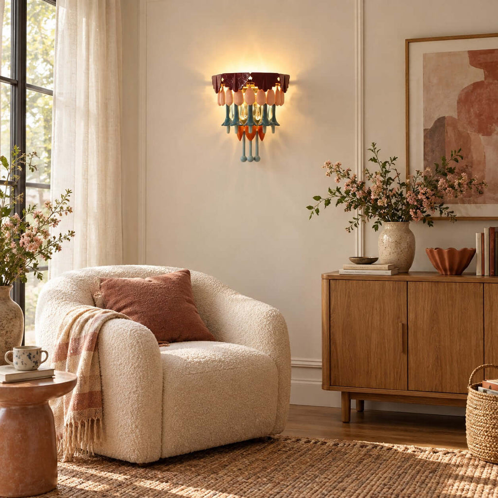 Clérachic wall sconce glowing near a sheer curtain, with a boucle armchair, a pink-blossom vase and a pale wood sideboard.