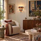 Living room with a Clérachic wall sconce beside colourful framed art, a cream armchair, a walnut cabinet and a round stone table.