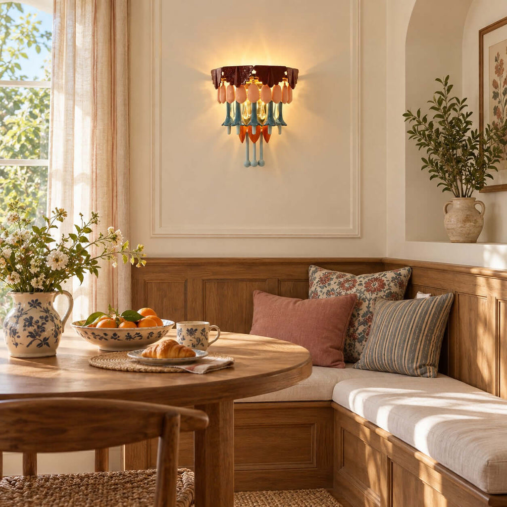 Breakfast nook with a Clérachic wall sconce above a built-in wooden bench, a round table with pastries and a jug of flowers.