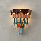 A Clérachic wall sconce lit against a grey plaster wall, showing its burgundy top, pink petals, teal stems and orange accents.